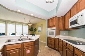 A modern kitchen with wooden cabinets, a microwave, an oven, and a sink. - Updated electronics in beachfront condo w/private balcony! (Destin)