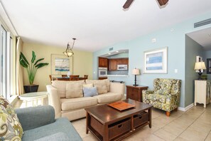A living room with a sofa, coffee table, and armchair, a dining area with a table and chairs, and a kitchen with cabinets and appliances. - Updated electronics in beachfront condo w/private balcony! (Destin)