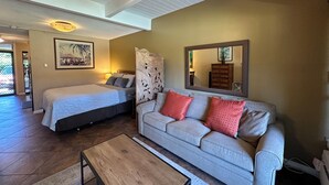 A room with a bed, a sofa, a ceiling fan, a mirror, and a wooden coffee table. - Kihei Bay Surf #119 Completely Remodeled Show Stopper! Shared Hot Tub, A/C (Kihei)