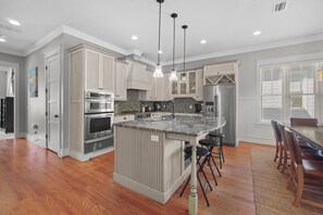 A modern kitchen with stainless steel appliances, a central island, pendant lighting, and a dining area with a wooden table and chairs.