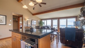 A spacious living area with a kitchen island, wooden flooring, and large windows offering ocean views.