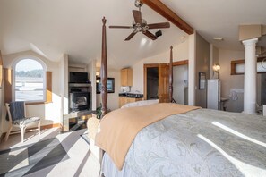 Une chambre dotée d’un grand lit, d’un ventilateur de plafond, d’une cheminée et offrant une vue sur l’extérieur.