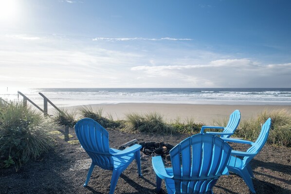 Une plage avec trois chaises bleues donnant sur l’océan, un foyer et un escalier en bois menant à la plage.