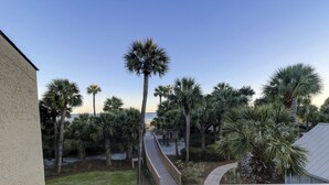 Un balcone con vista su palme e un percorso che conduce a una spiaggia.