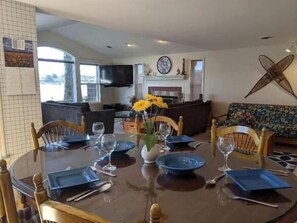 A dining area with a round table set for four, surrounded by wooden chairs. A vase with yellow flowers is placed on the table.