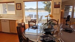 Un comedor con vistas a la playa, una cocina equipada con lavavajillas y una mesa de comedor dispuesta con platos, vasos y cubiertos.