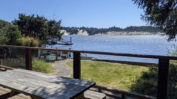 Una terraza de madera con una mesa de picnic que da a una masa de agua, un muelle y un promontorio boscoso.