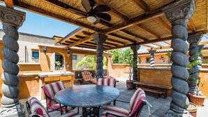 An outdoor patio with a round table and striped chairs, surrounded by stone columns and a thatched roof. - Villa Buho✰Rooftop Jacuzzi & Private Pool ✰Across from Beach (Tamarindo)