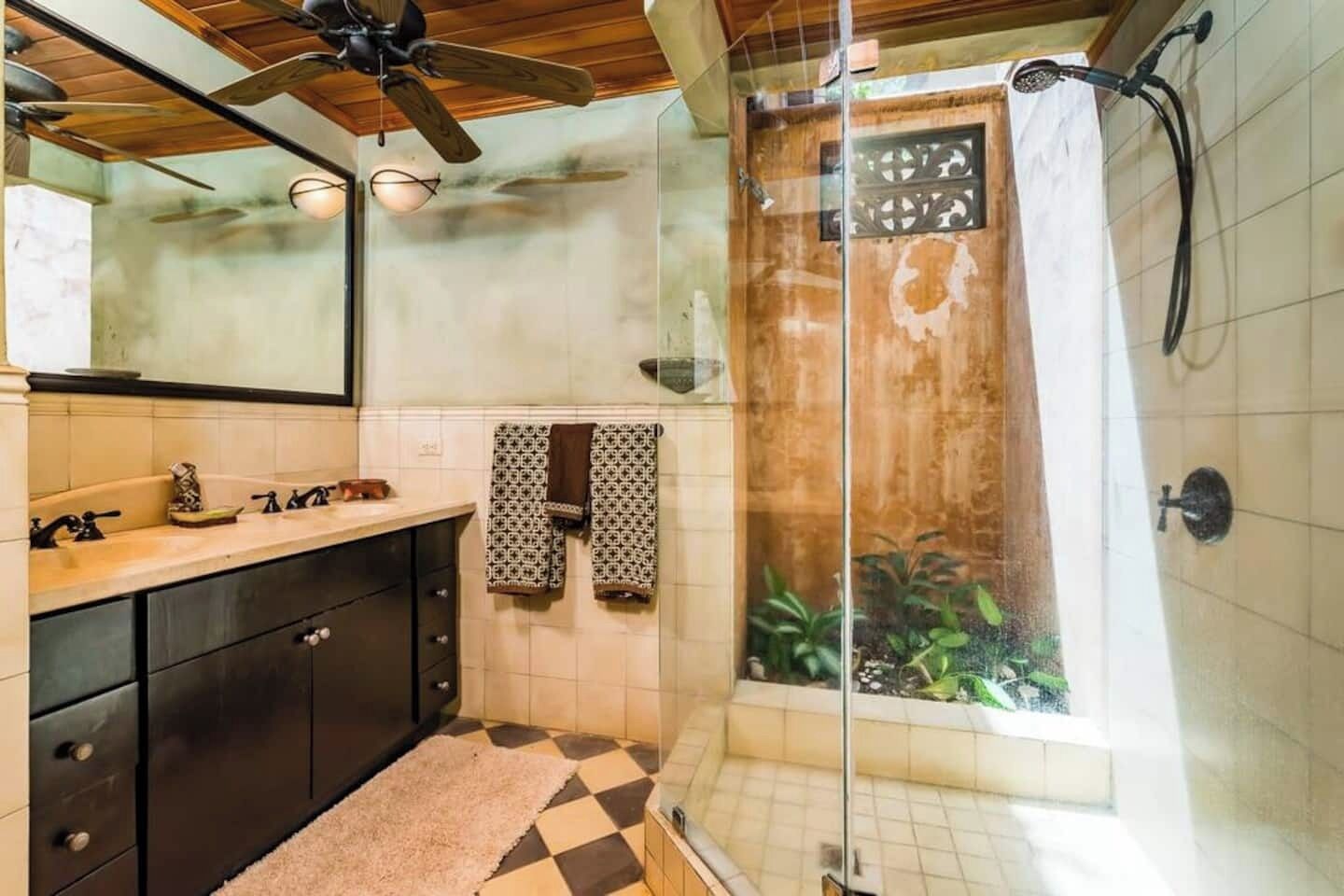Une salle de bain équipée d’une douche, d’un lavabo, d’un miroir et d’un ventilateur de plafond.
