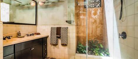 Une salle de bain équipée d’une douche, d’un lavabo, d’un miroir et d’un ventilateur de plafond.