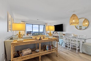 Relax in a spacious living room with a sofa, dining table, and wall-mounted TV, offering a view of the outdoors.