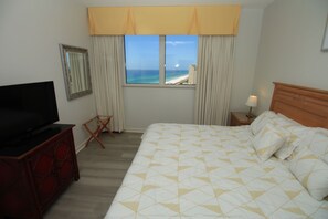 Ein Hotelzimmer mit Bett, Fernseher, Sessel, Nachttisch und Fenster mit Meerblick.