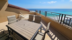 A balcony with a wooden table and chairs, a view of the ocean, and a railing. - 4828 Beachfront 3BR | 16th Floor | Two Masters | Private Beach + Tram Access (Miramar Beach)