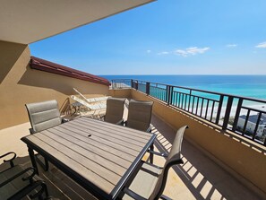 A balcony with a wooden table and chairs, a view of the ocean, and a railing.