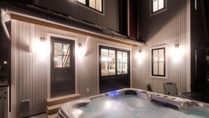 Ein Whirlpool in einer überdachten Außenbereich mit Holzwänden und -türen, sowie ein kleiner Tisch und Stuhl in der Nähe.
