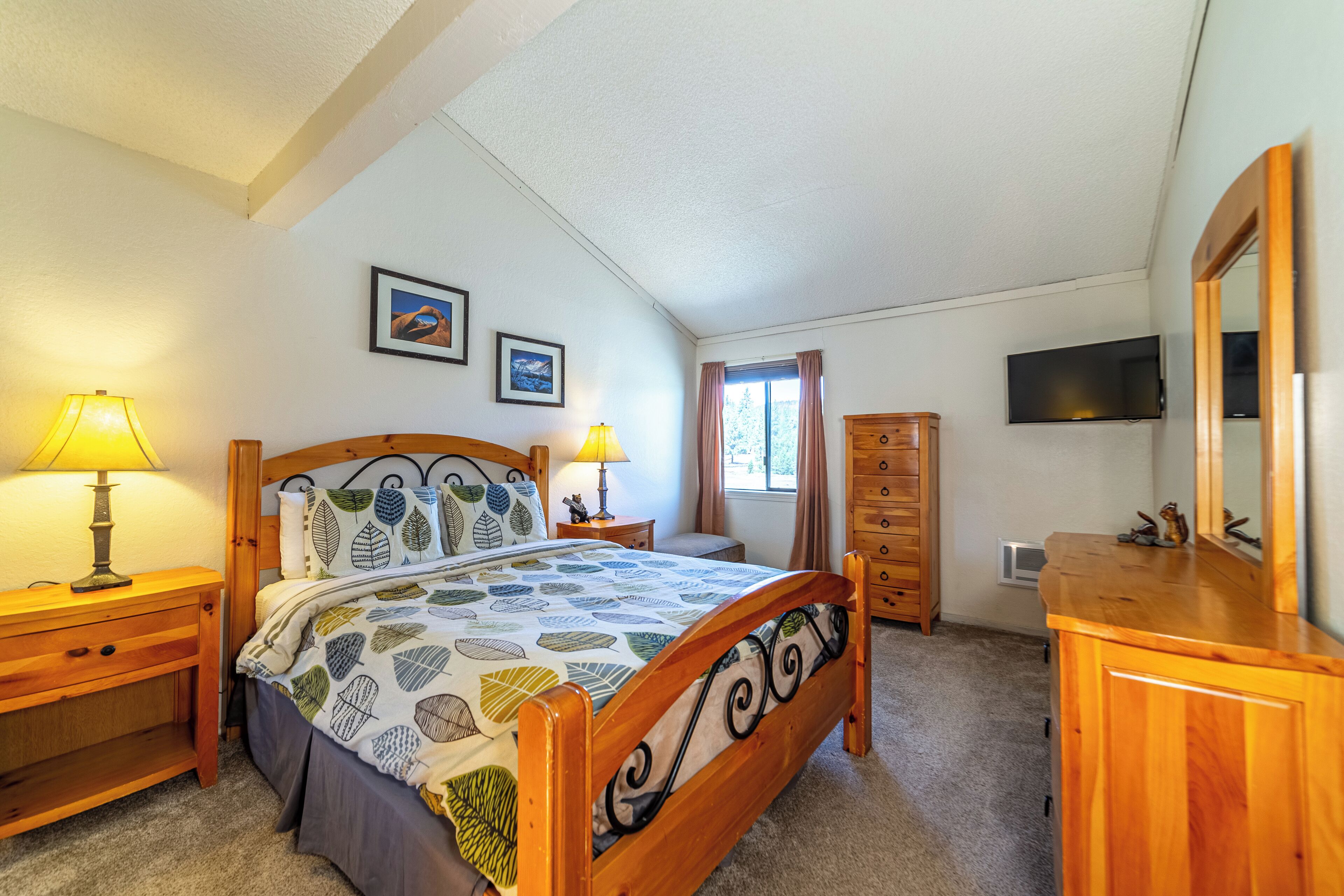 Une chambre à coucher comprenant un lit, des tables de chevet, une commode, un miroir et un téléviseur.