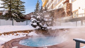 A hot tub surrounded by snow, with a stone wall and a wooden fence. - ✲ Ski In / Ski Out | Zephyr Mountain Lodge 2413 | Updated Condo | Views of Divide (Winter Park)