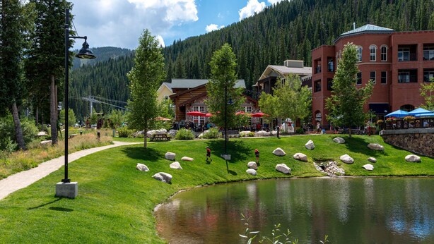 A riverside park with a pond, picnic tables, and a red-roofed building with outdoor seating. - ✲ Ski In / Ski Out | Zephyr Mountain Lodge 2413 | Updated Condo | Views of Divide (Winter Park)