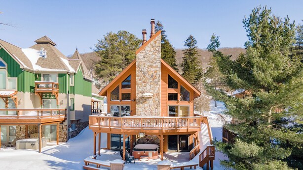 Un'ampia lodge a più piani con camino in pietra, balconi in legno e una terrazza coperta di neve con posti a sedere all'aperto.
