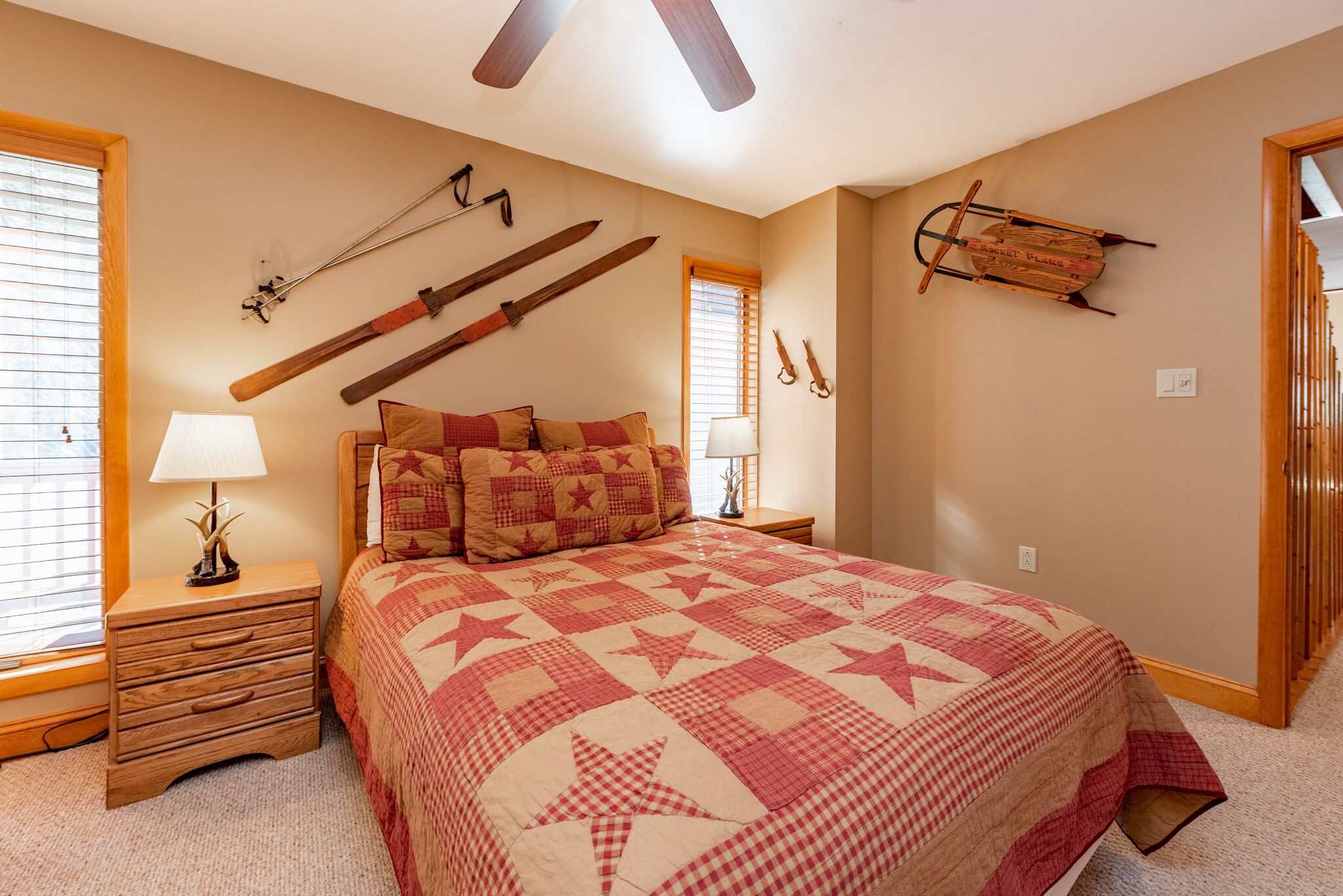 A bedroom with a large bed, wooden nightstands, a ceiling fan, and wall-mounted skis and a sled.