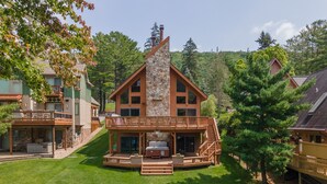 Un'ampia baita a più piani in legno con un camino in pietra, una veranda con posti a sedere all'aperto e una scala che conduce al piano superiore.