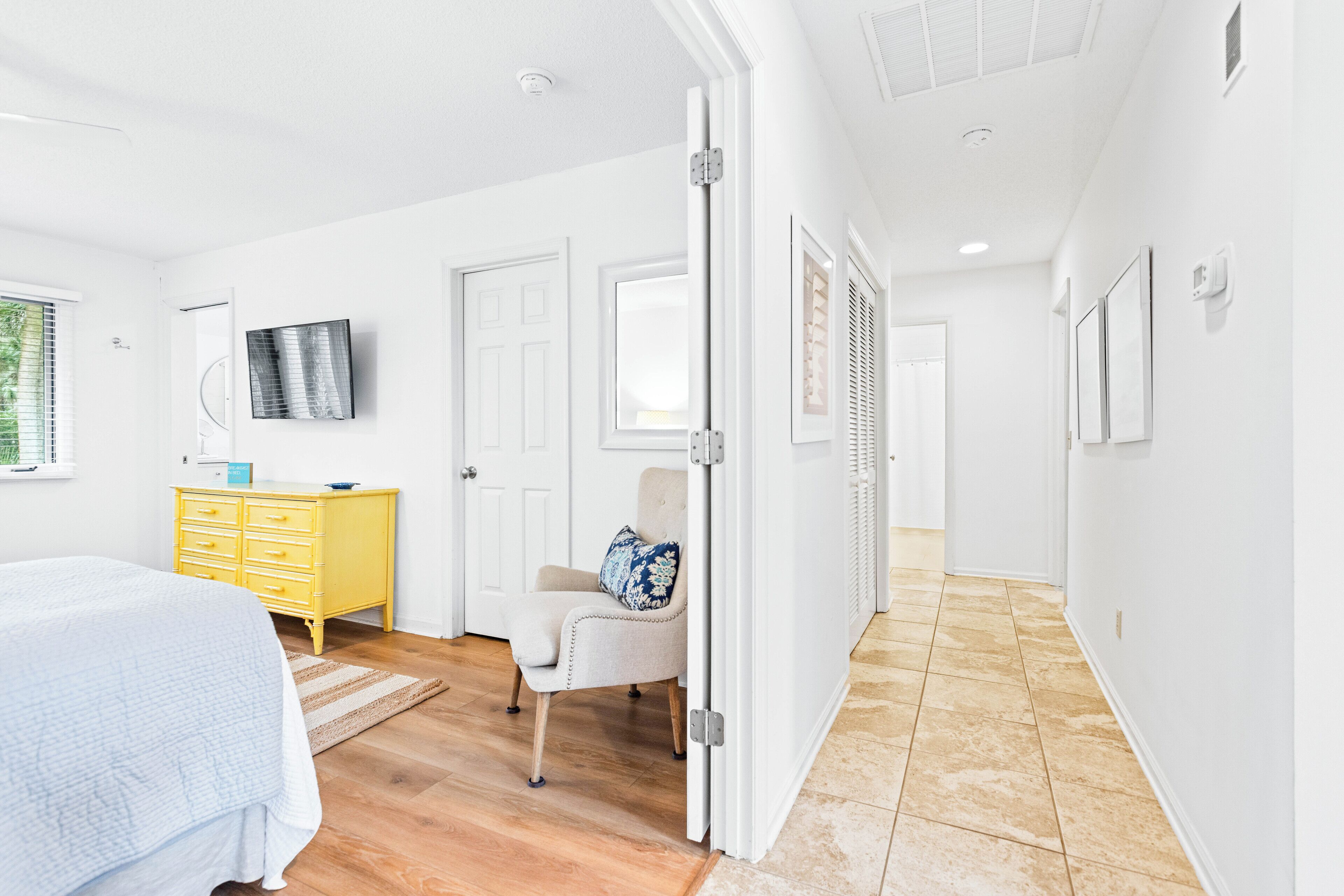 A bedroom with a bed, a yellow dresser, a chair, and a television on the wall.