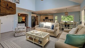 Un salon spacieux avec un plafond haut, un ventilateur de plafond et un coin repas offrant une vue sur la verdure.