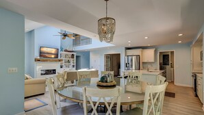 Un vaste espace de vie comprenant un coin repas avec une table ronde, des chaises blanches et un ventilateur de plafond.