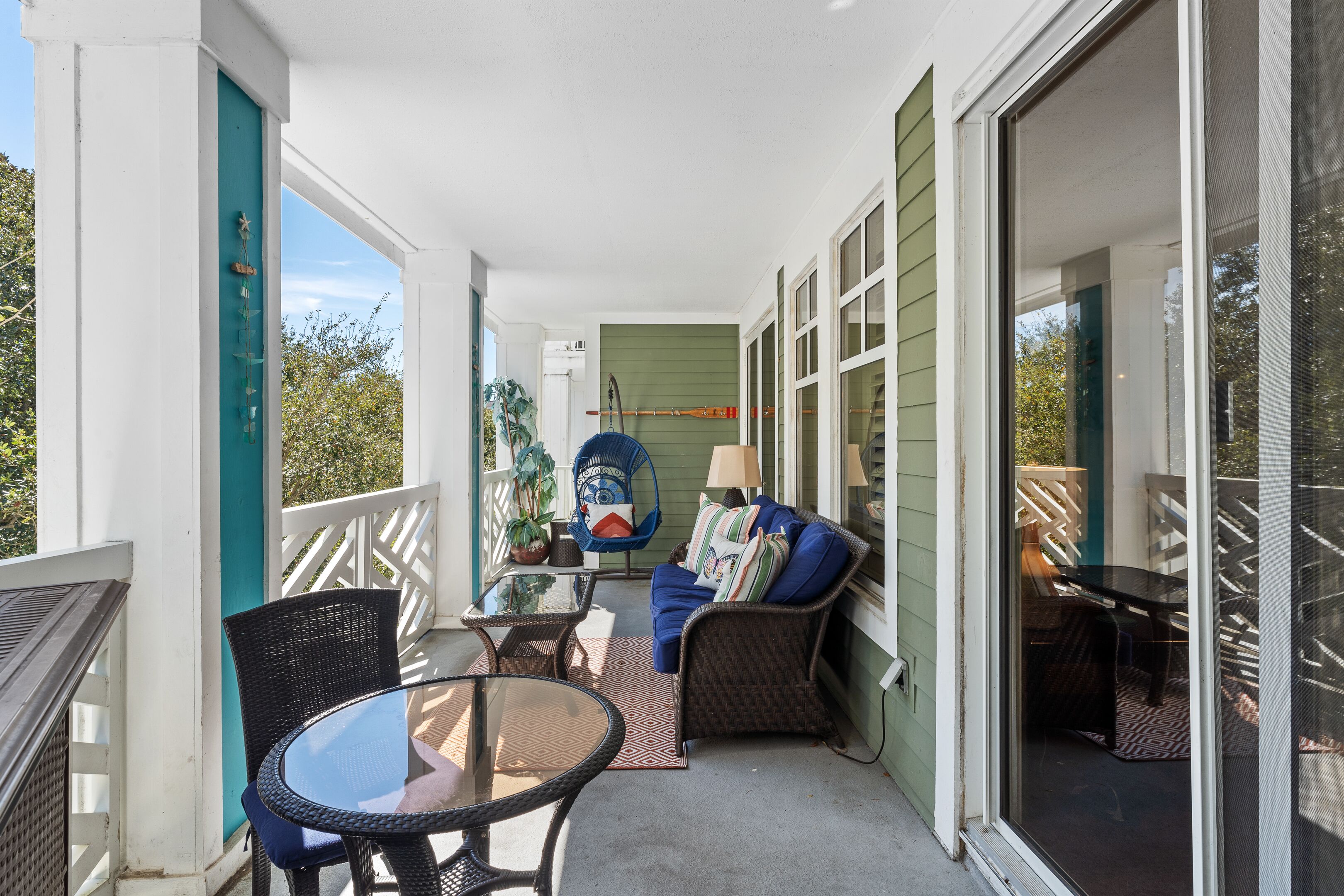 A covered porch with wicker furniture, a glass table, and a blue chair.