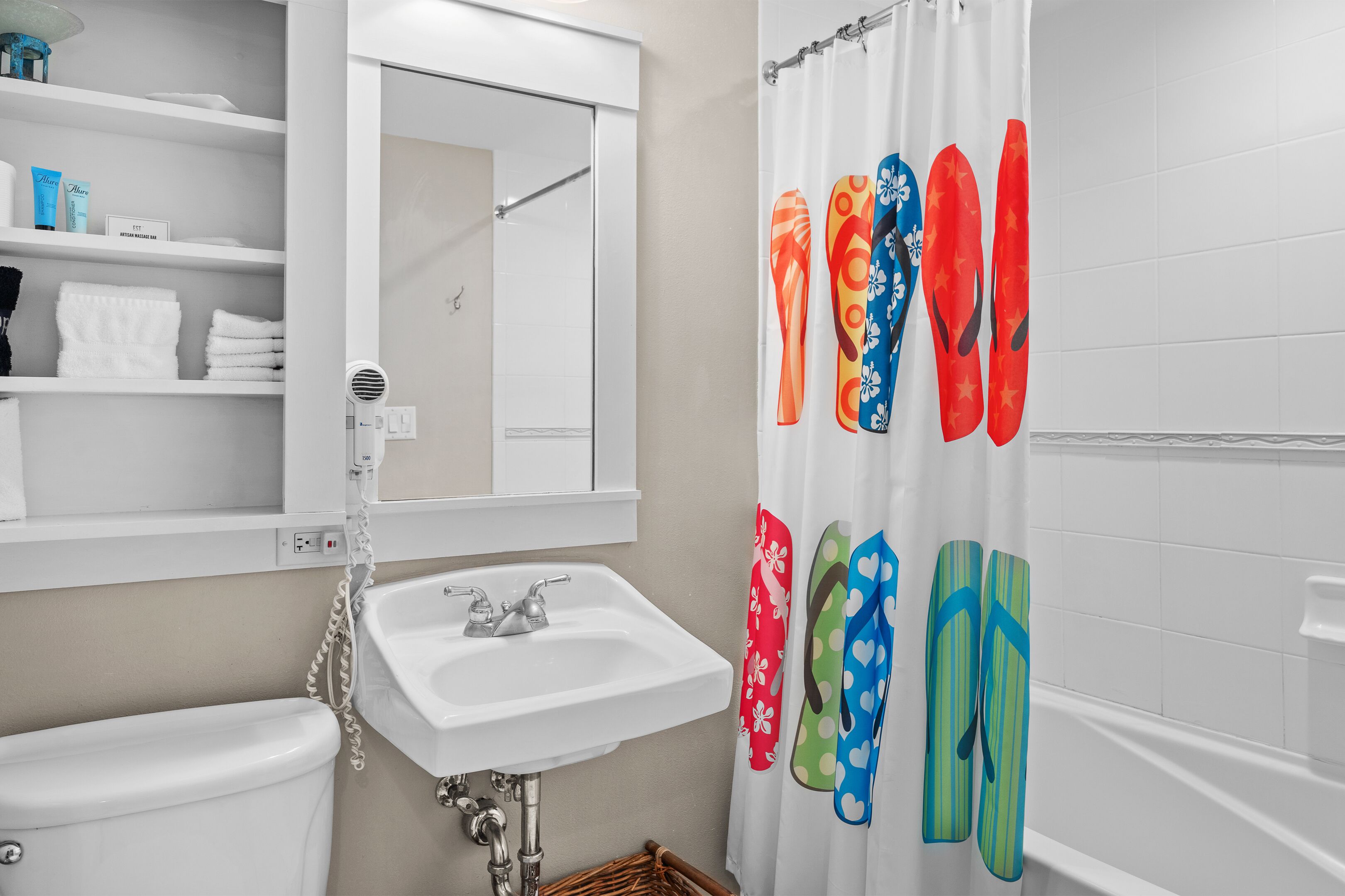 A bathroom with a white sink, mirror, and toilet. There are colorful bath slippers hanging on the wall.