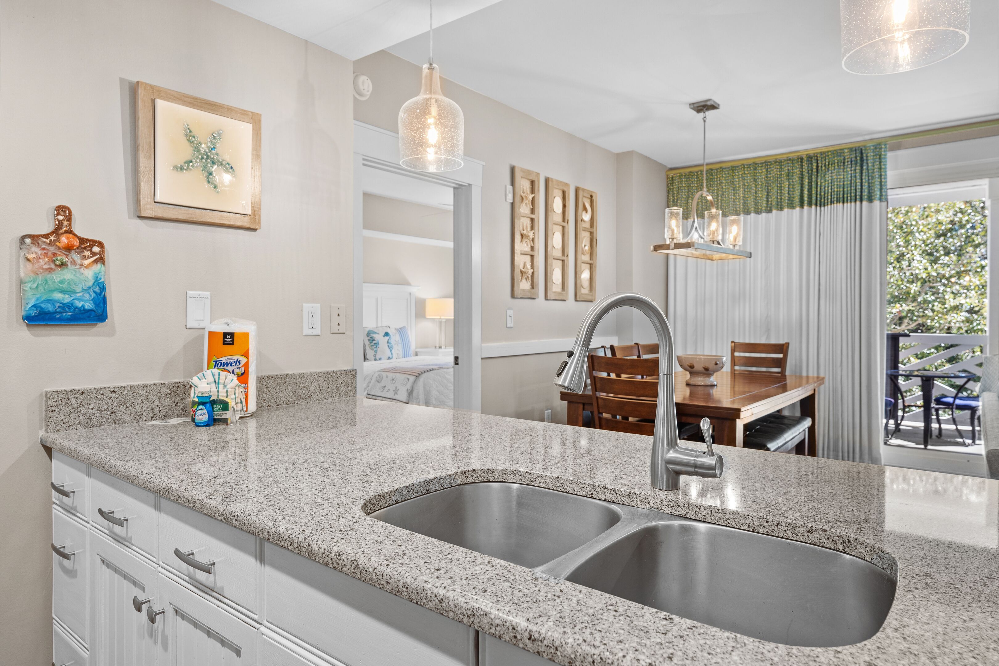 A kitchen with granite countertops, a double sink, and a dining area with a wooden table and chairs.