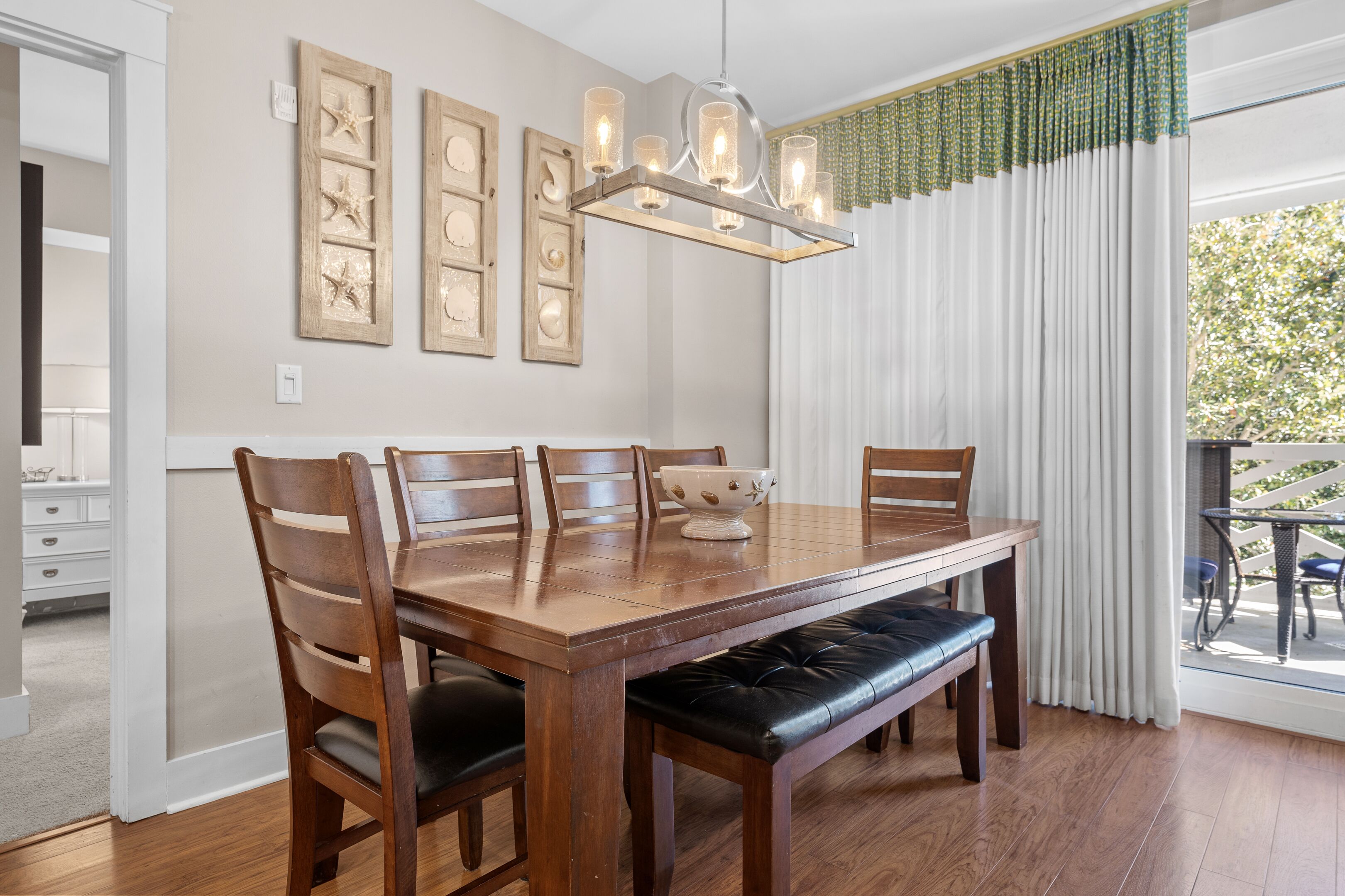 A dining area with a wooden table, six chairs, a bench, a chandelier, and framed artwork on the wall.