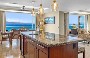 A modern kitchen with a large island, a dining area with chairs, and a view of the ocean.