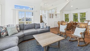 Ein geräumiges Wohnzimmer mit einem grauen Ecksofa, Holzschaukelstühlen und einem Couchtisch aus Holz.