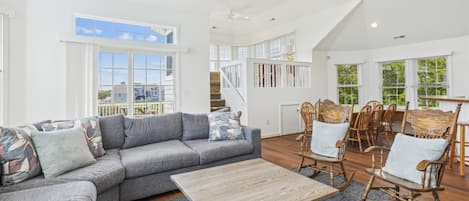 Uma sala de estar espaçosa com um sofá modular cinza, poltronas de balanço de madeira e uma mesa de centro de madeira.