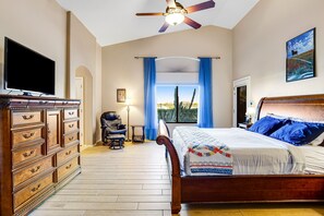 Une chambre à coucher avec un lit, une commode en bois, un ventilateur de plafond et une fenêtre avec des rideaux.