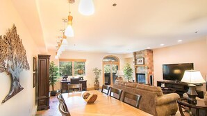 A spacious living room with a wooden dining table, comfortable seating, a flat-screen TV, and a stone fireplace. - Spacious Renovated 2-Bedroom Mountain Village Escape (Mountain Village)