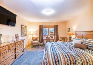 Una habitación de hotel con una cama grande, un escritorio, una silla, un televisor y una ventana con cortinas.