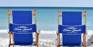 Two beach chairs with "Silver Beach Towers" branding, positioned on a sandy beach with the ocean in the background.