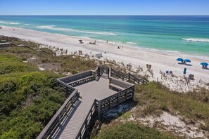 A beach with a wooden boardwalk leading to a sandy area with umbrellas and beach chairs.