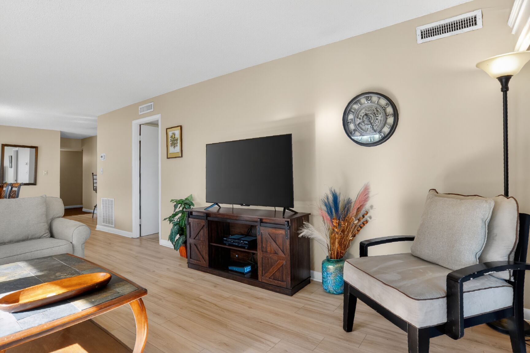 Una sala de estar con una televisión de pantalla plana, una mesa de centro de madera, un sofá, un sillón y un jarrón decorativo.