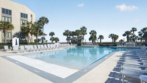 A swimming pool with lounge chairs, palm trees, and a building in the background.