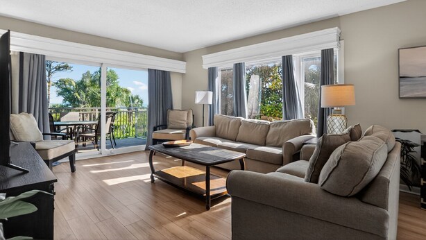A spacious living area with a sofa, armchairs, a coffee table, and a balcony with outdoor furniture.