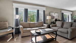 A living room with a sofa set, a coffee table, a lamp, and a view of greenery outside.