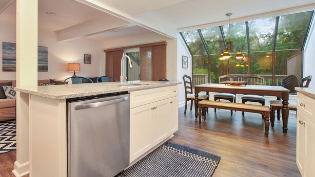 Una cocina moderna con lavavajillas integrado, un comedor con mesa y sillas de madera, y un ventanal que ofrece vistas al exterior.