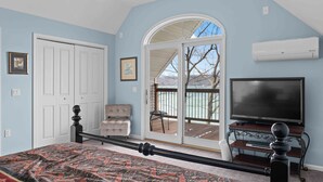 A bedroom with a bed, a television, a sliding glass door, and a ceiling fan.