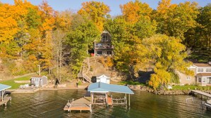 A lakeside property with a dock, a small cabin, and a larger house with a balcony overlooking the water.