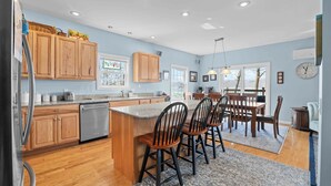 A kitchen with wooden cabinets, a stainless steel refrigerator, a granite countertop, and a dining area with wooden chairs and a table.