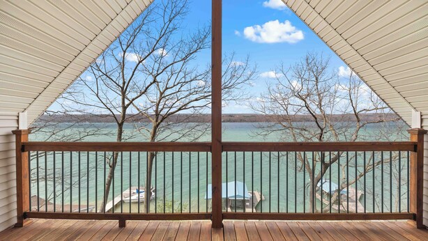 A wooden deck with a view of a lake and boats, a metal railing, and a clear sky.