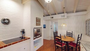 A kitchen with a stove, a microwave, and a vent. There is a dining table with chairs and a hanging light fixture.